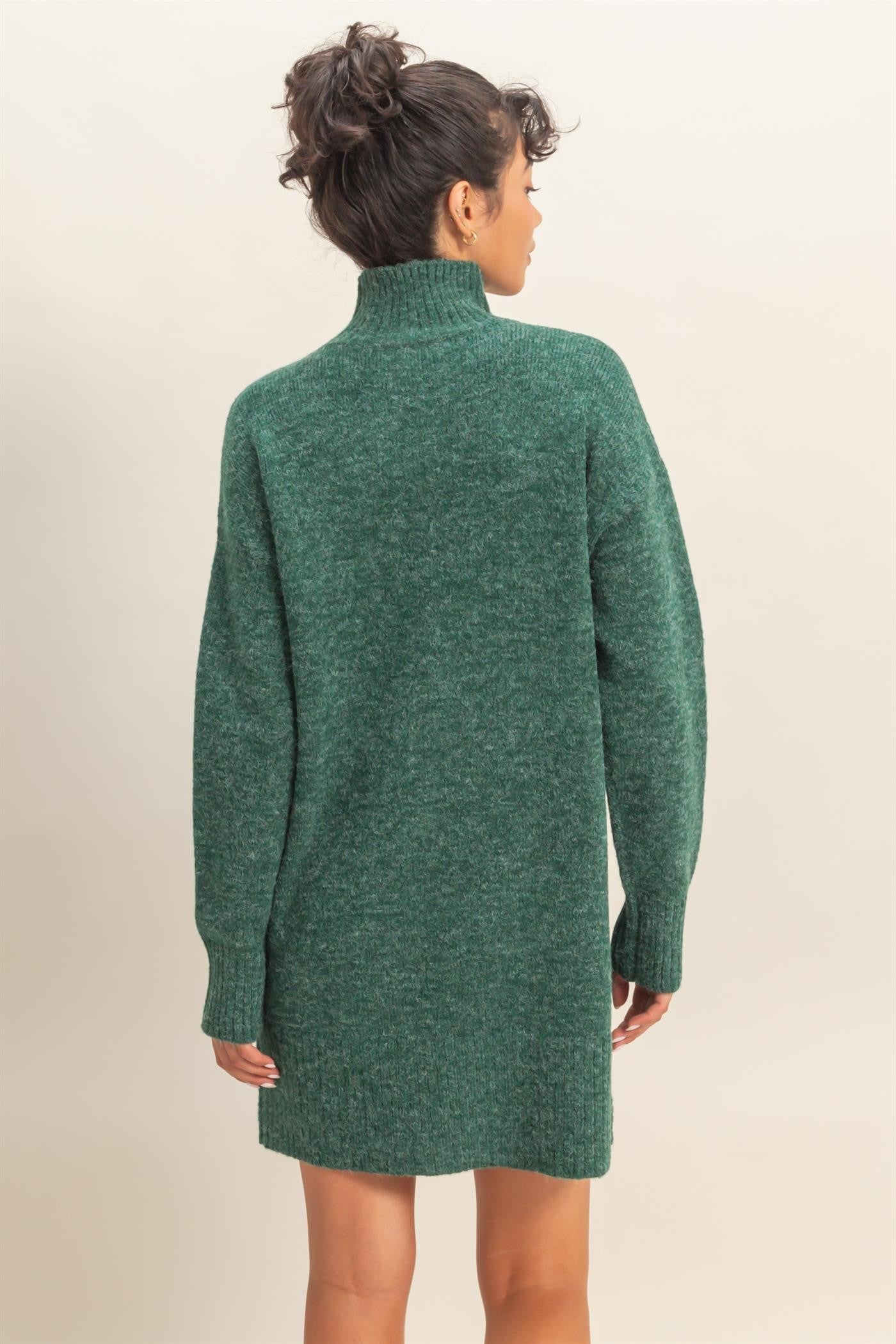 woman wearing a green oversized sweater dress with a high collar and long sleeves, viewed from the back