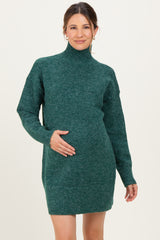 woman wearing a dark green maternity sweater dress with a high neck and relaxed fit, holding her baby bump
