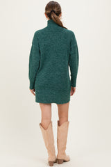 woman wearing a dark green maternity sweater dress with a high neck and long sleeves, styled with knee-high beige boots