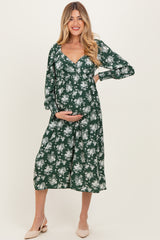 woman wearing a green floral maternity dress and holding her baby bump