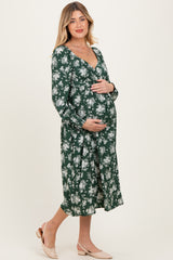 woman wearing a green floral maternity dress with long sleeves and holding her baby bump