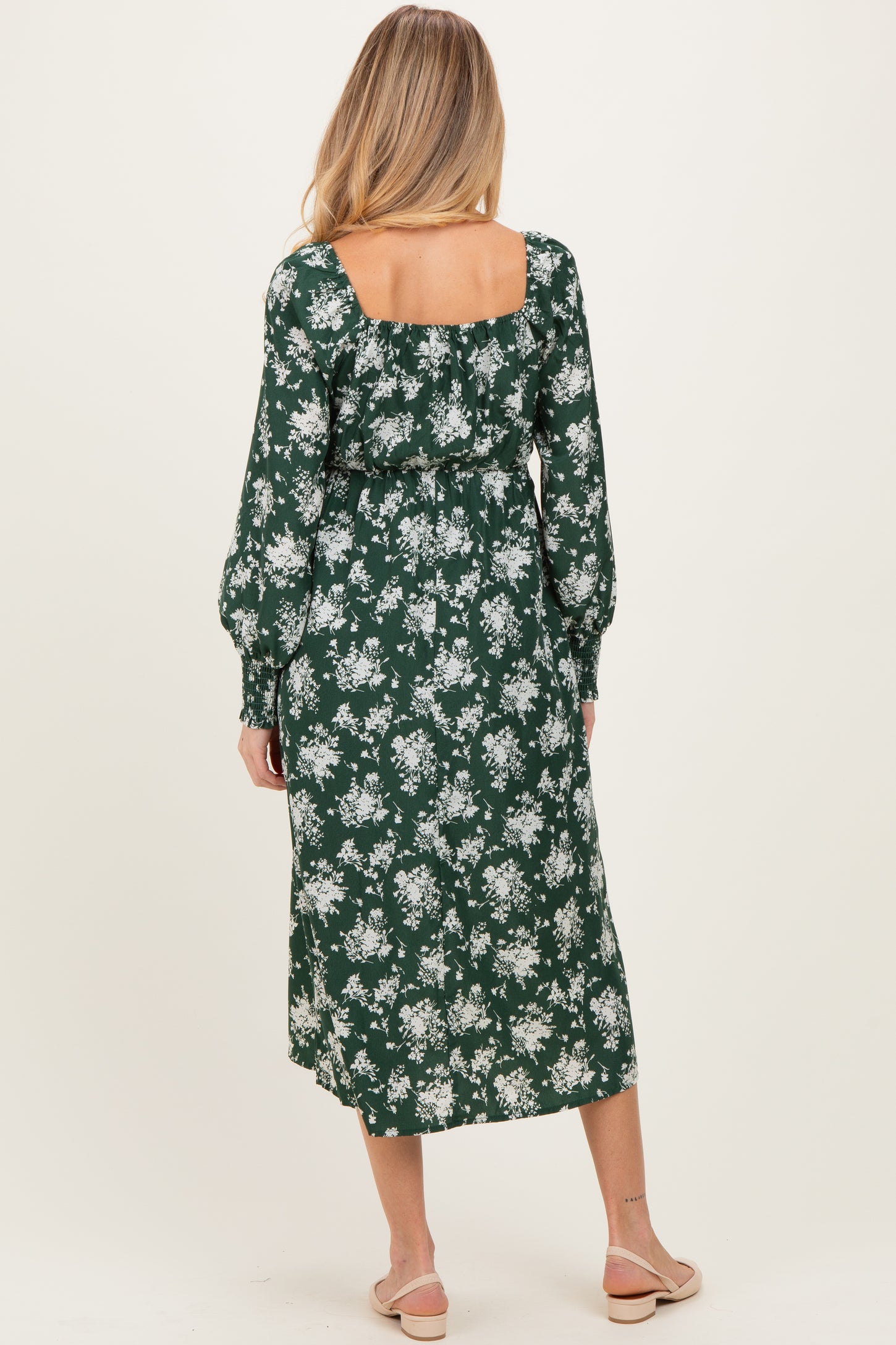 woman wearing a green floral maternity dress with long sleeves and a square neckline, showing a baby bump