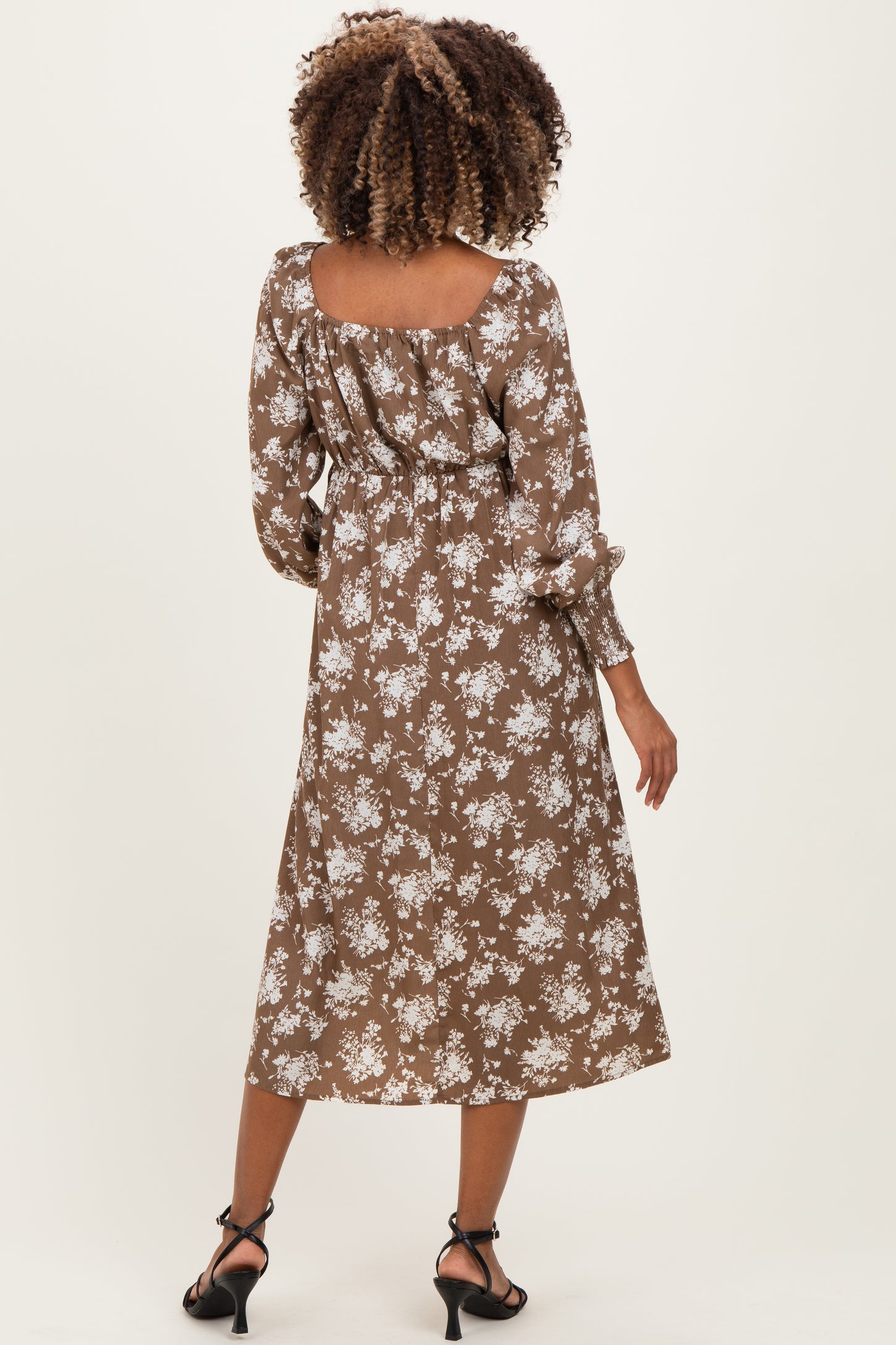 woman wearing a brown floral maternity dress with long sleeves and a flowy silhouette, showing a baby bump