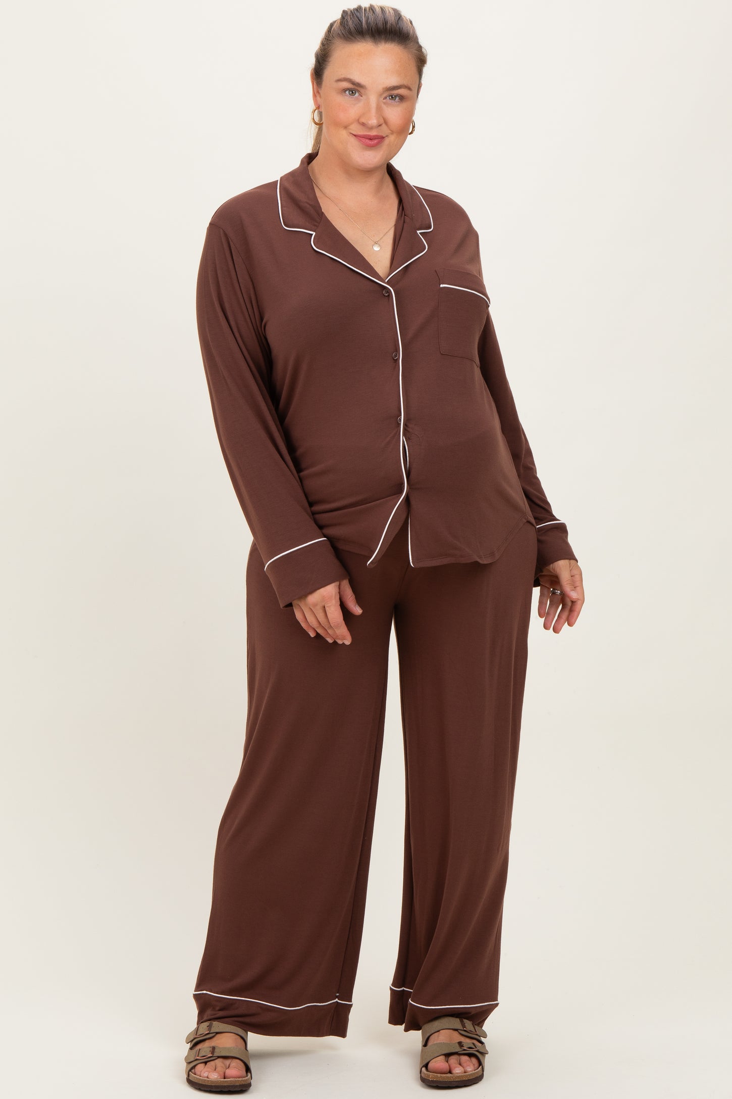 woman wearing a brown maternity plus size pajama set with white piping and a visible baby bump