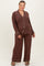 woman wearing a brown maternity plus size pajama set with white piping and a visible baby bump
