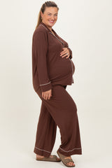 woman wearing a brown maternity plus pajama set with white piping and holding her baby bump
