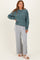 woman wearing a teal oversized sweatshirt and light gray wide-leg pants with soft slippers on her feet