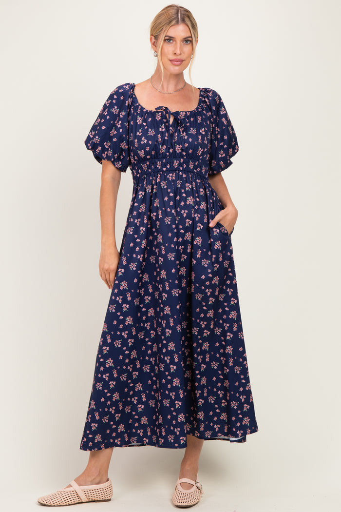 woman wearing a navy blue floral maxi dress with puff sleeves and a cinched waist, posing with hands in pockets