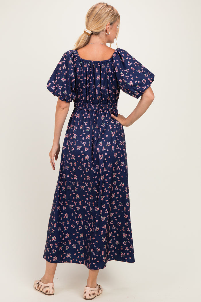 woman wearing a navy blue floral maxi dress with puff sleeves and a smocked waist, shown from the back