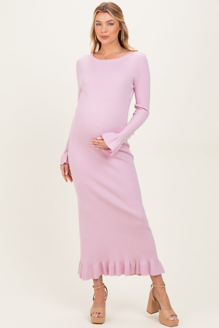 woman wearing a light pink ribbed maternity dress with long sleeves and ruffled hem, gently cradling her baby bump