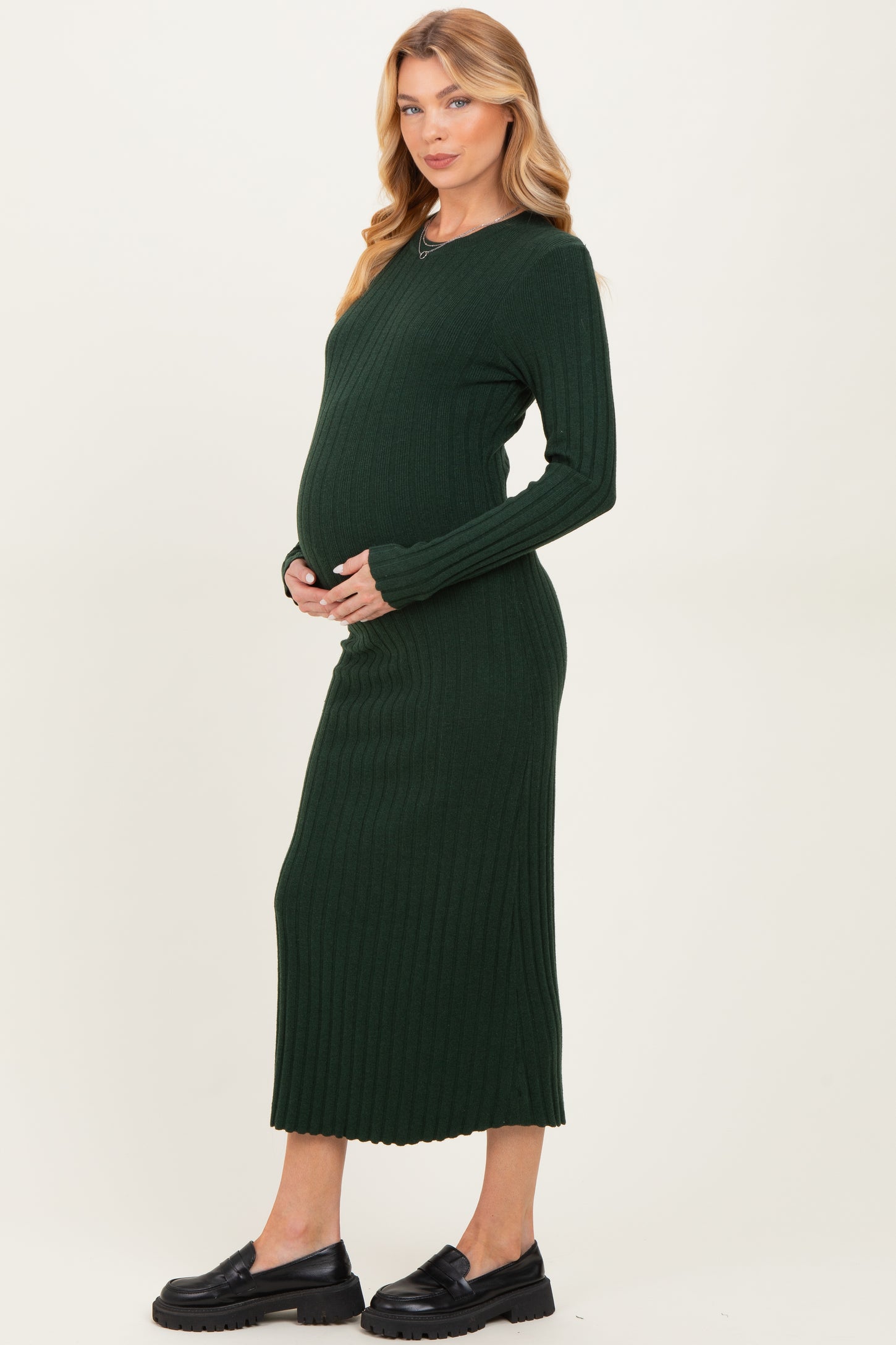 woman wearing a dark green ribbed long sleeve maternity dress and cradling her baby bump