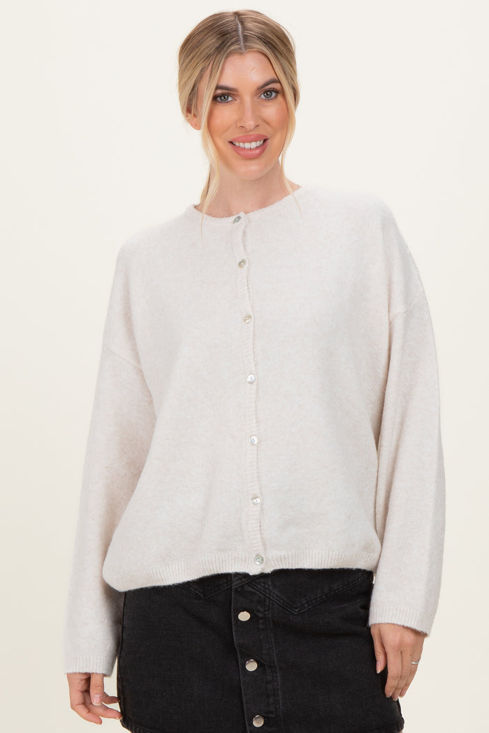 woman wearing a light beige oversized cardigan with pearl buttons and black denim skirt