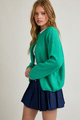 woman wearing a bright green oversized cardigan and a denim pleated mini skirt