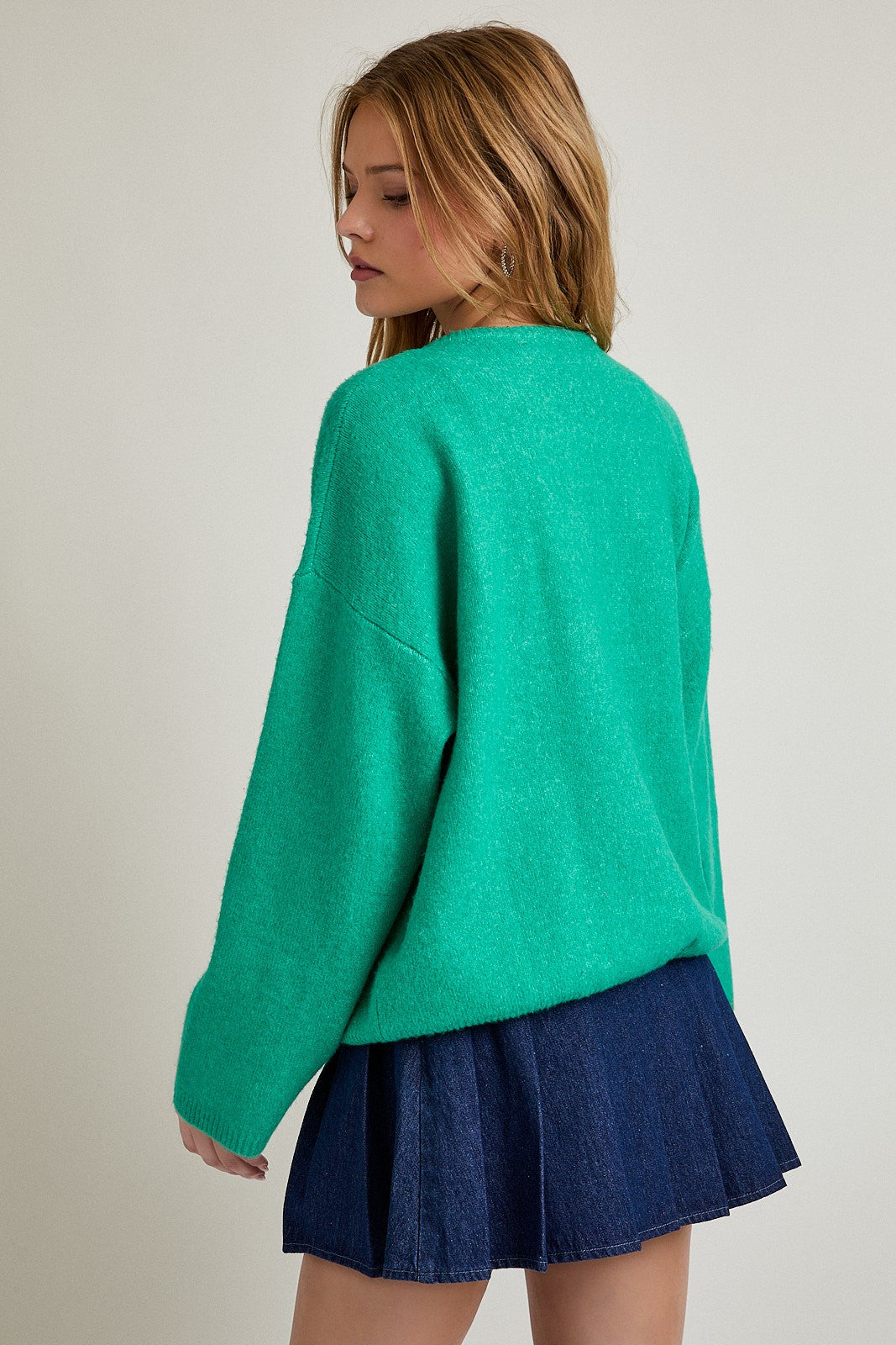 woman wearing a green oversized sweater and a denim mini skirt, viewed from the back