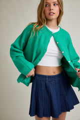 woman wearing a green cardigan over a white crop top and a denim pleated skirt