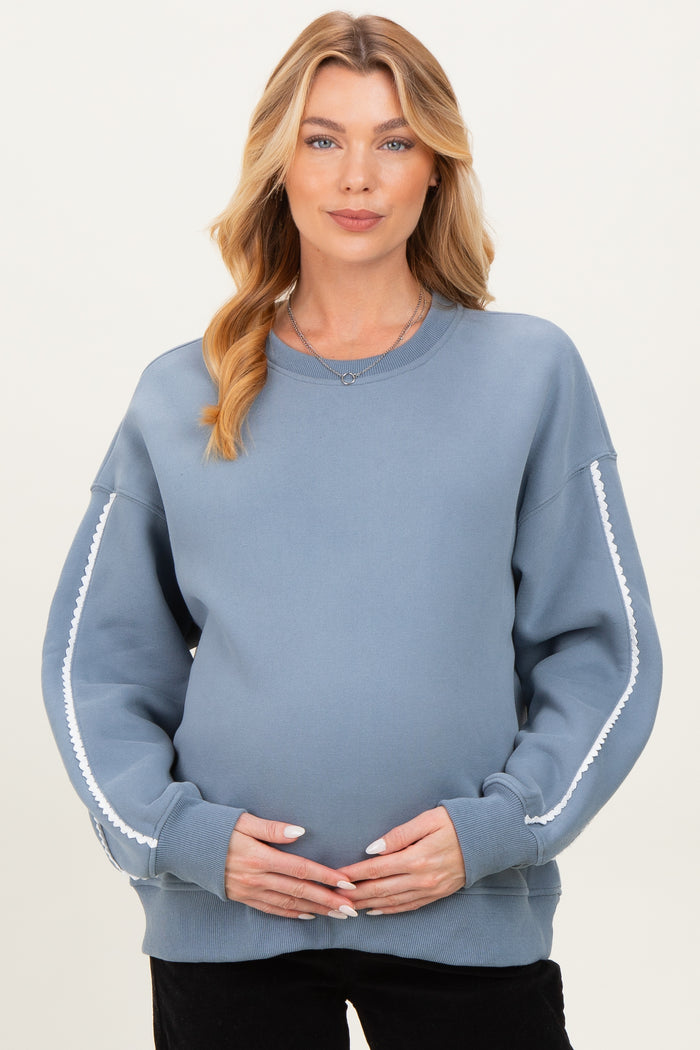 woman wearing a blue maternity sweatshirt with decorative white trim and holding her baby bump