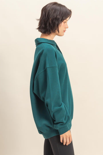woman wearing an oversized teal sweatshirt with a collar and long sleeves, styled casually against a light background
