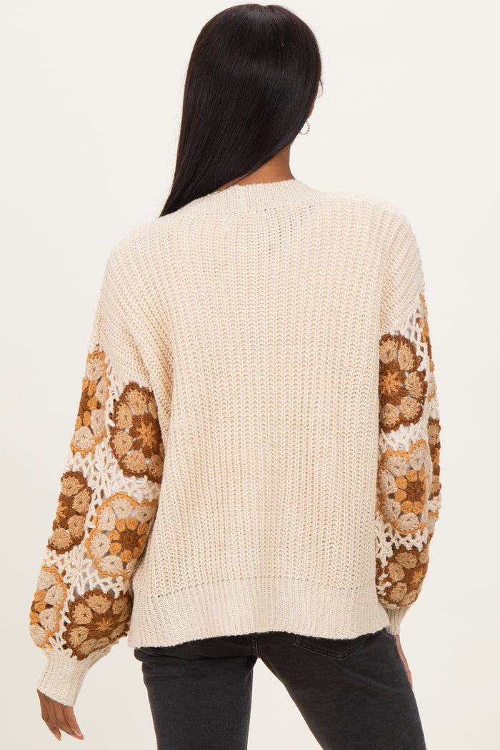 woman wearing a cream-colored knit sweater with floral patterned sleeves and a relaxed fit