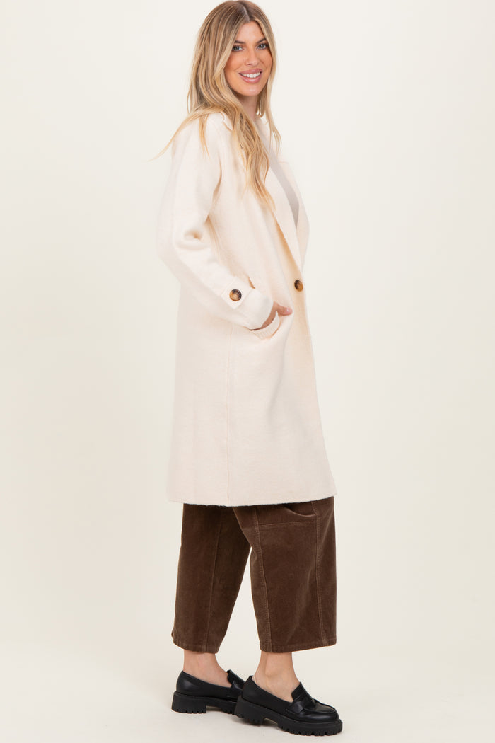 woman wearing a long cream-colored cardigan with buttons and side pockets, paired with brown corduroy pants and black shoes