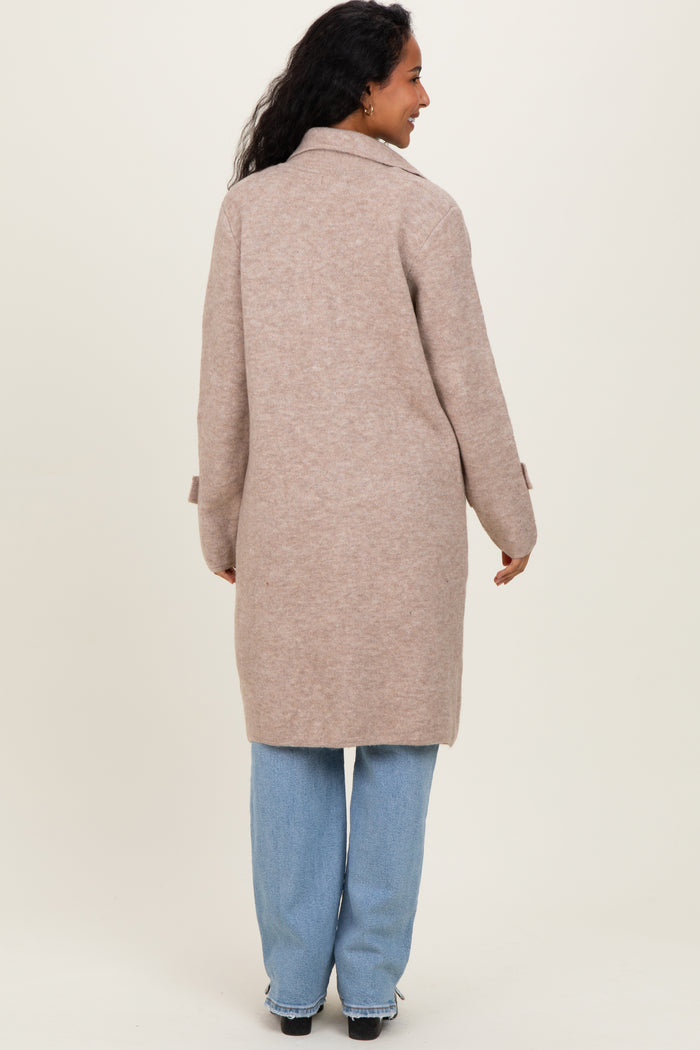woman wearing a beige maternity coat with a relaxed fit and long sleeves, styled with light blue jeans
