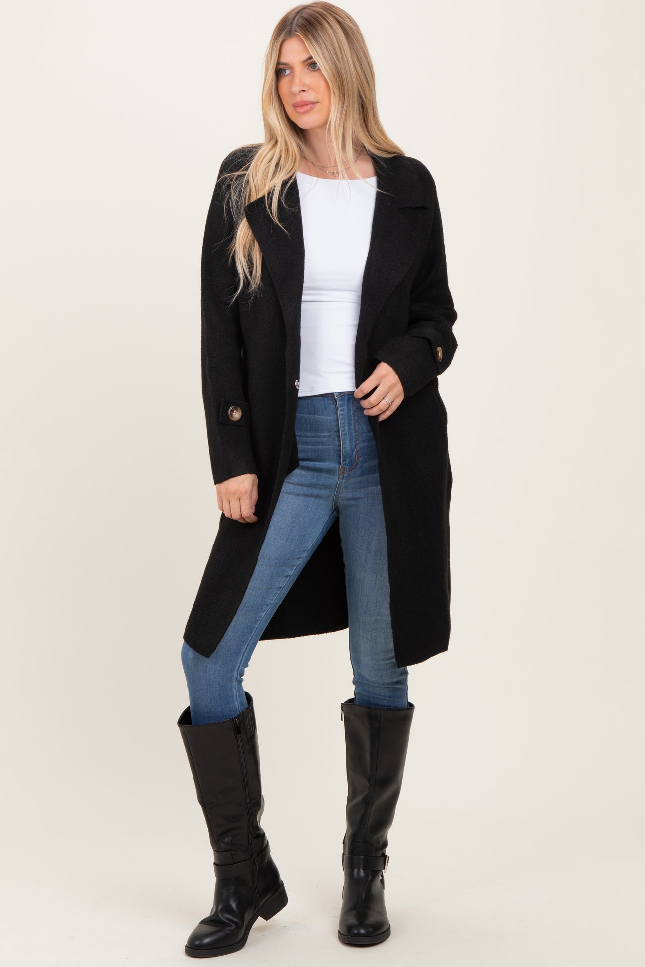 woman wearing a black long coat over a white top and blue jeans, paired with black knee-high boots