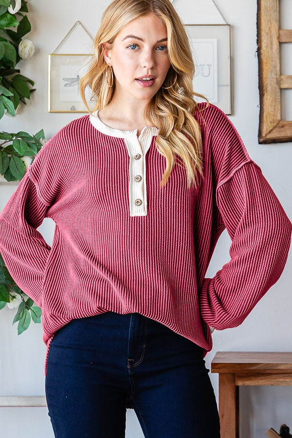 woman wearing a burgundy ribbed long sleeve top with a white button placket and relaxed fit, styled with dark jeans