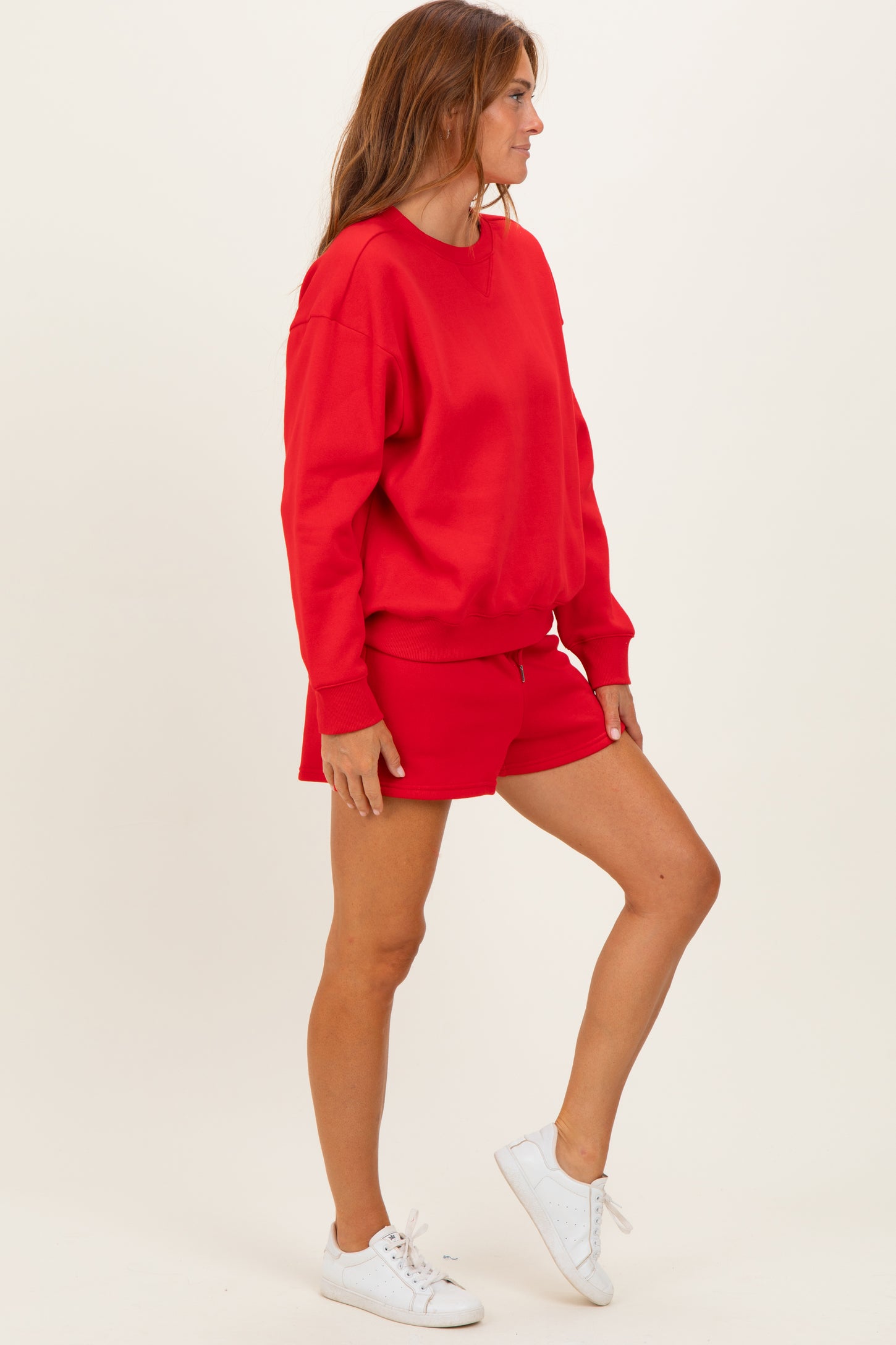 woman wearing a red oversized sweatshirt and matching red shorts with white sneakers