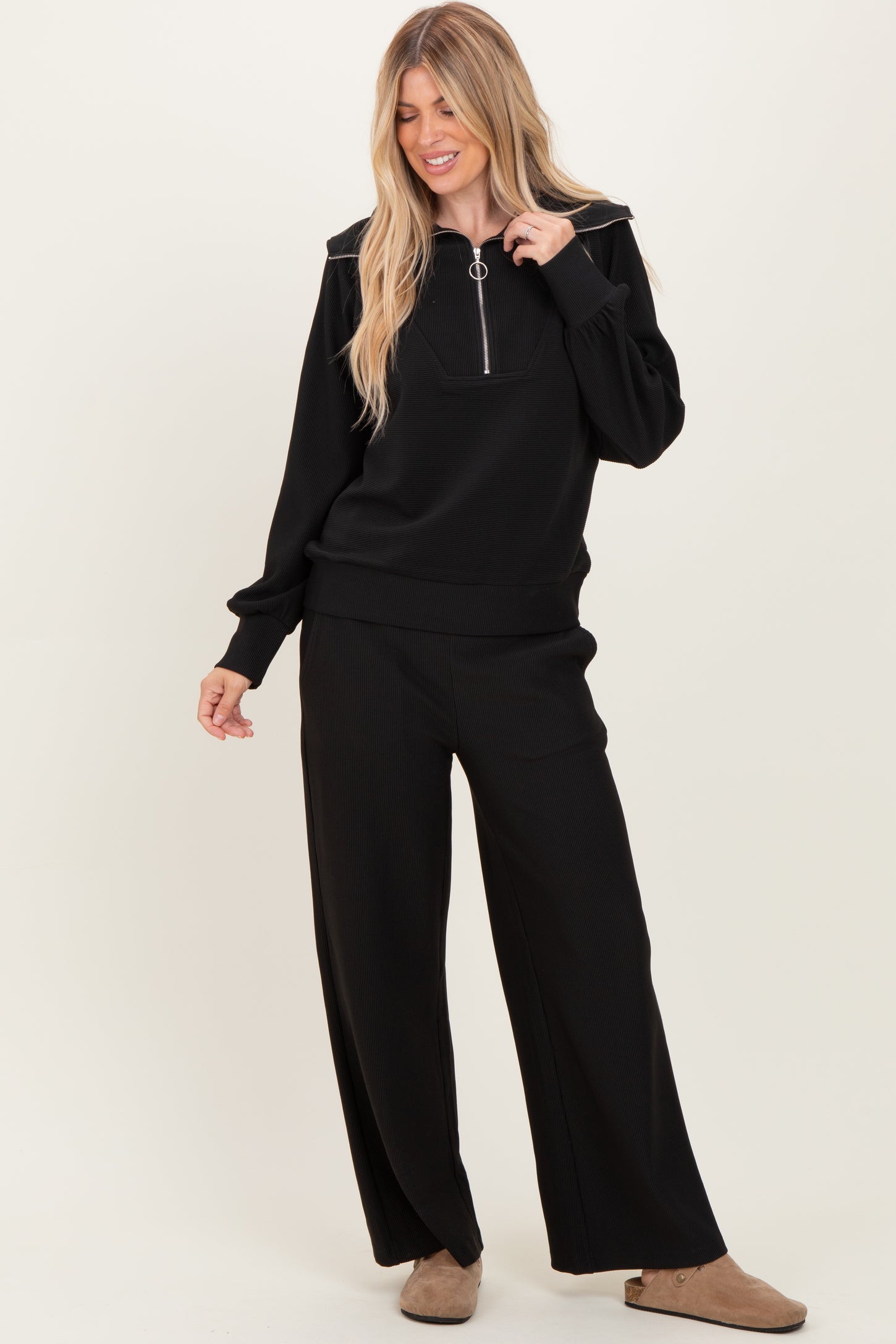 woman wearing a black ribbed zip-up sweater and matching wide-leg pants, styled casually with beige slip-on shoes