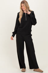 woman wearing a black ribbed zip-up sweater and matching wide-leg pants, styled casually with beige slip-on shoes
