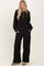 woman wearing a black long sleeve zip-up top with a collar and matching wide-leg black pants.