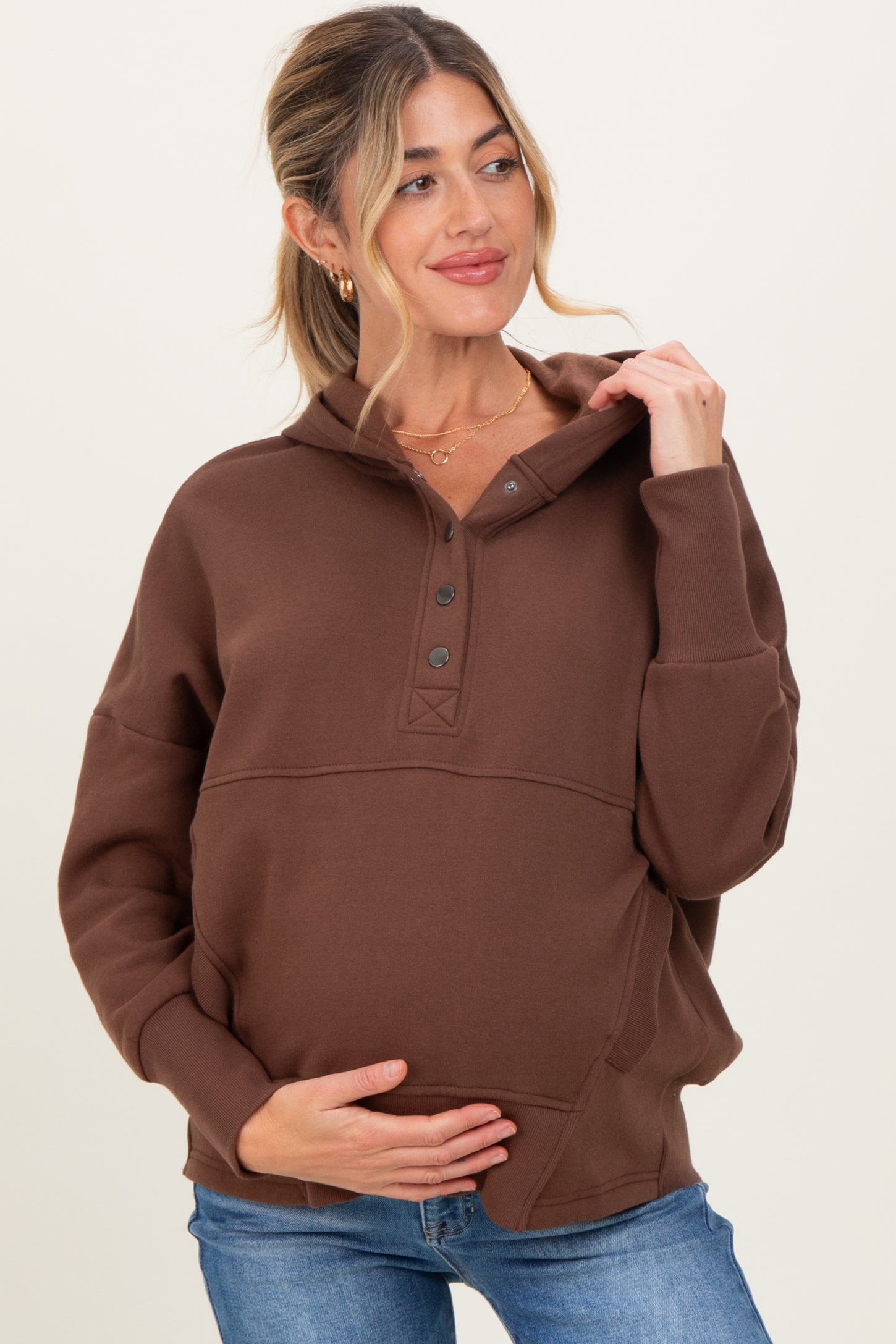 woman wearing a brown maternity hoodie with buttons, holding her baby bump