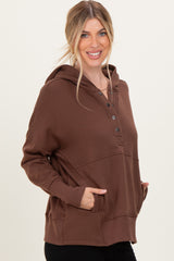woman wearing a brown hooded sweatshirt with button accents and front pockets