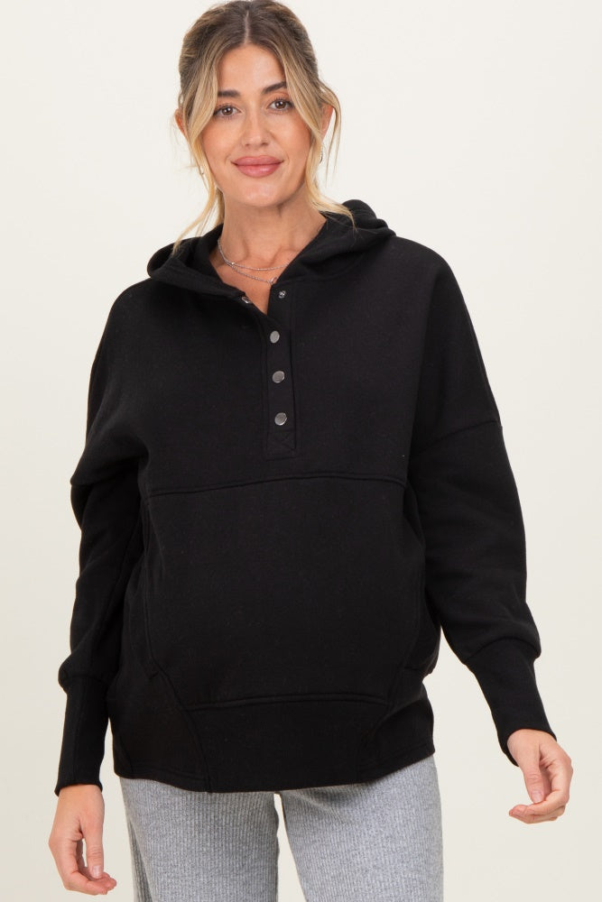 woman wearing a black maternity hoodie with a buttoned neckline and a relaxed fit, showing her baby bump