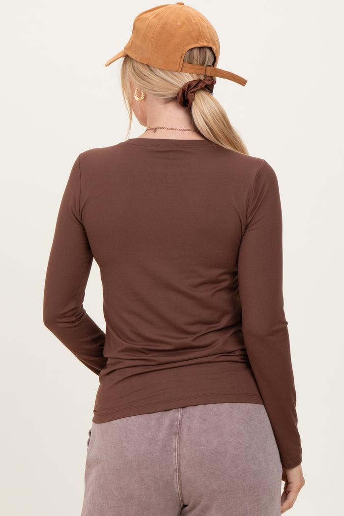 woman wearing a form-fitting brown long sleeve top, viewed from the back, with a brown cap and styled hair