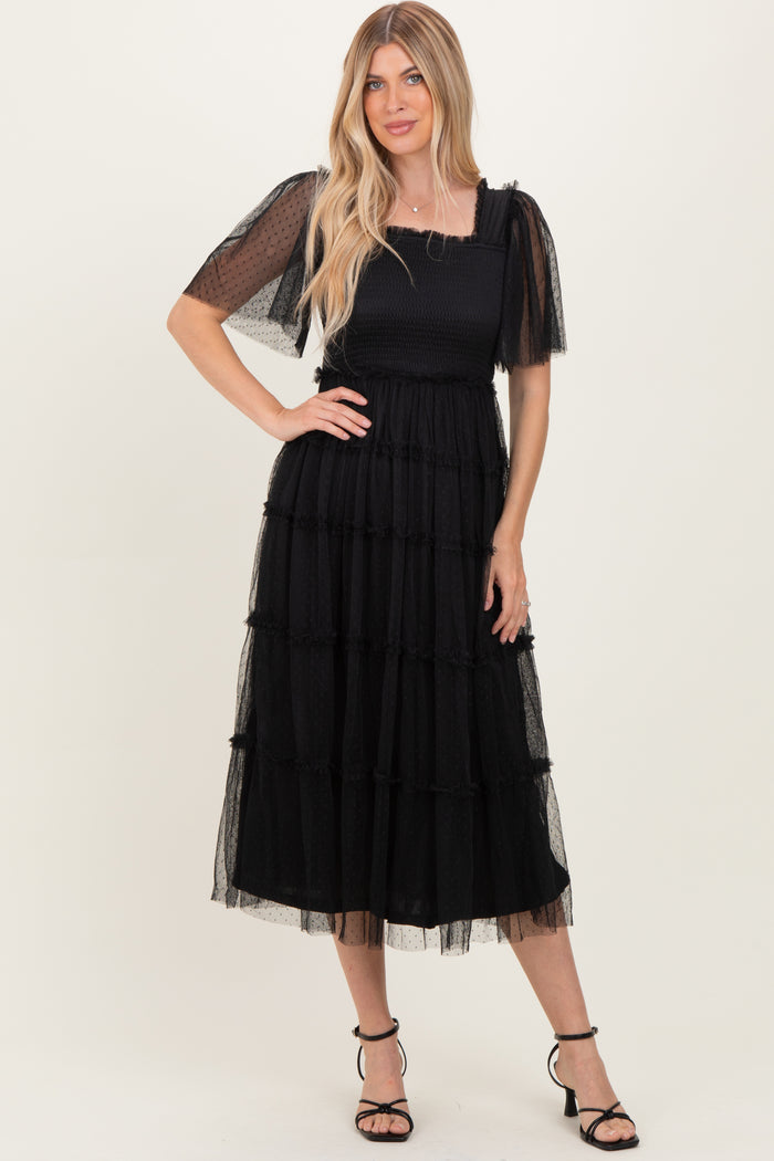 woman wearing a black tiered midi dress with puff sleeves and a square neckline, standing confidently