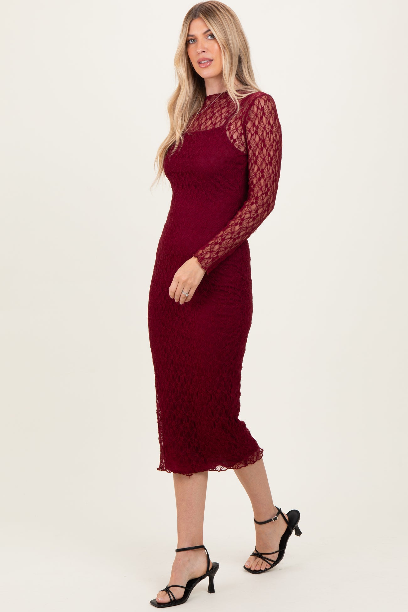 woman wearing a burgundy lace long sleeve midi dress with a fitted silhouette and side slit, paired with black heels