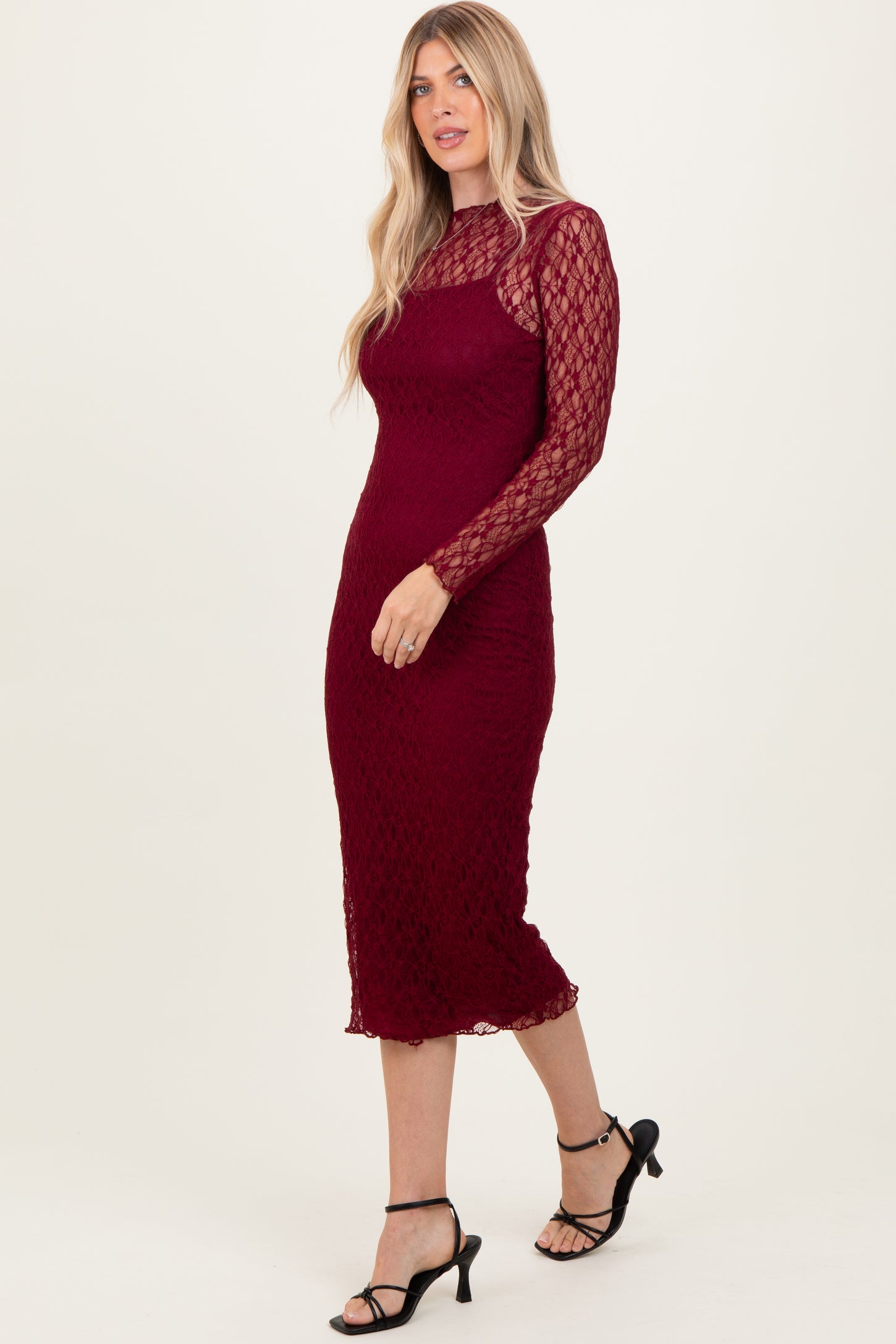 woman wearing a burgundy lace long sleeve midi dress with a fitted silhouette and side slit, paired with black heels