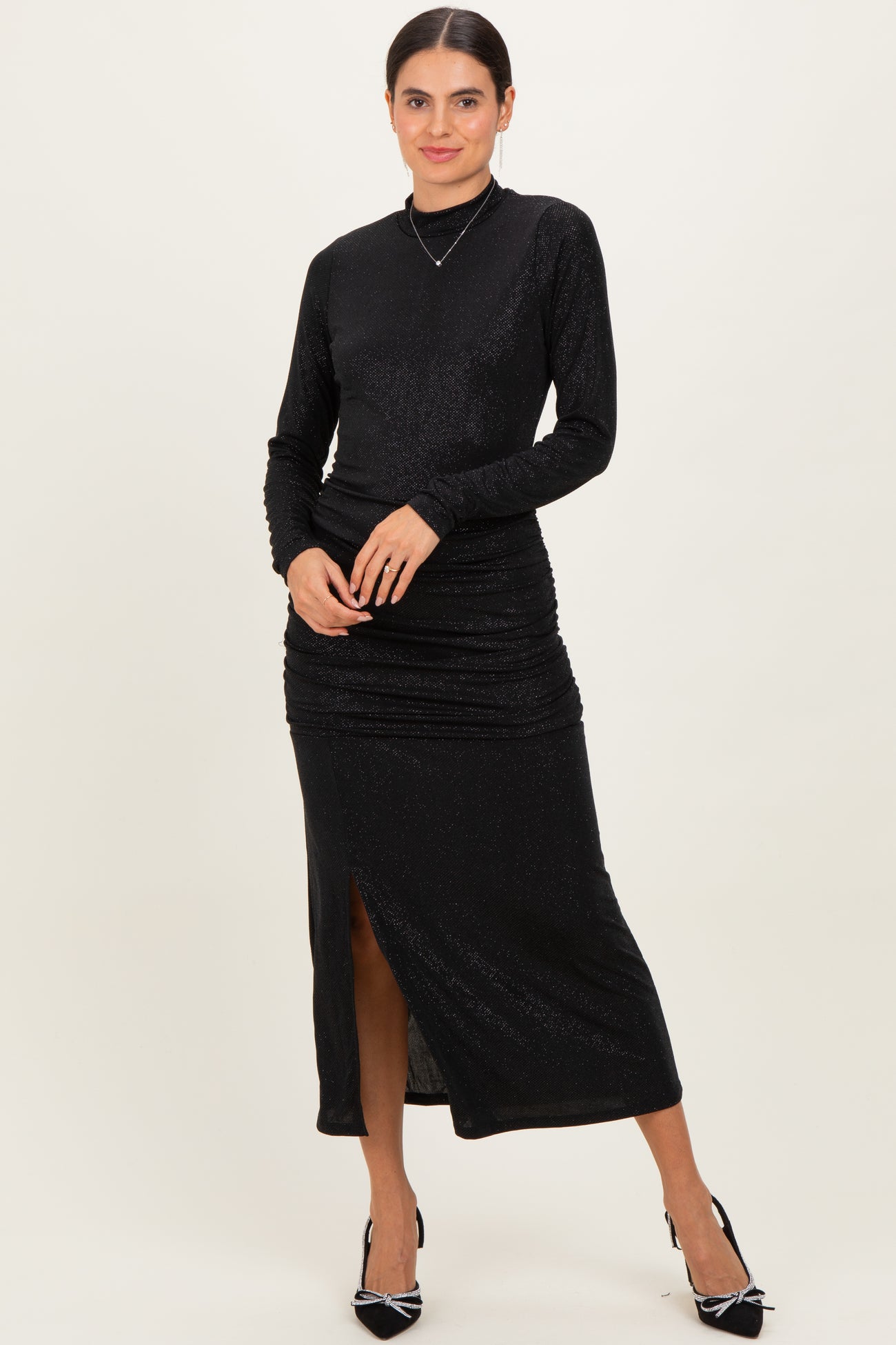 woman wearing a black long sleeve shimmer dress with a side slit and ruched detailing