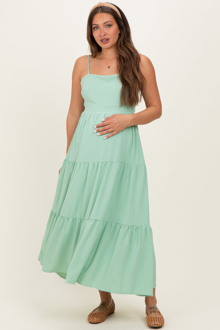 woman wearing a mint green maternity maxi dress with tiered ruffles and holding her baby bump