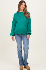 woman wearing a teal maternity sweater with balloon sleeves and light blue jeans, smiling at the camera
