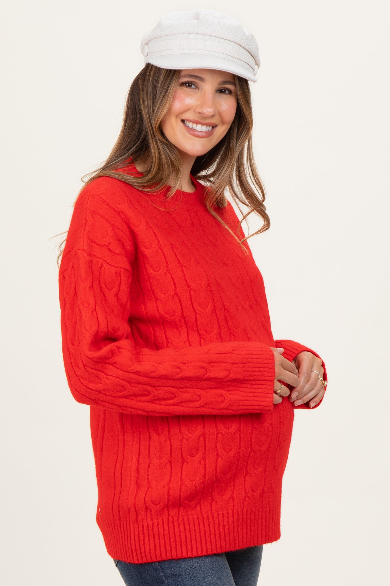 woman wearing a red cable knit maternity sweater and holding her baby bump