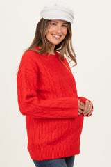 woman wearing a red cable knit maternity sweater and holding her baby bump