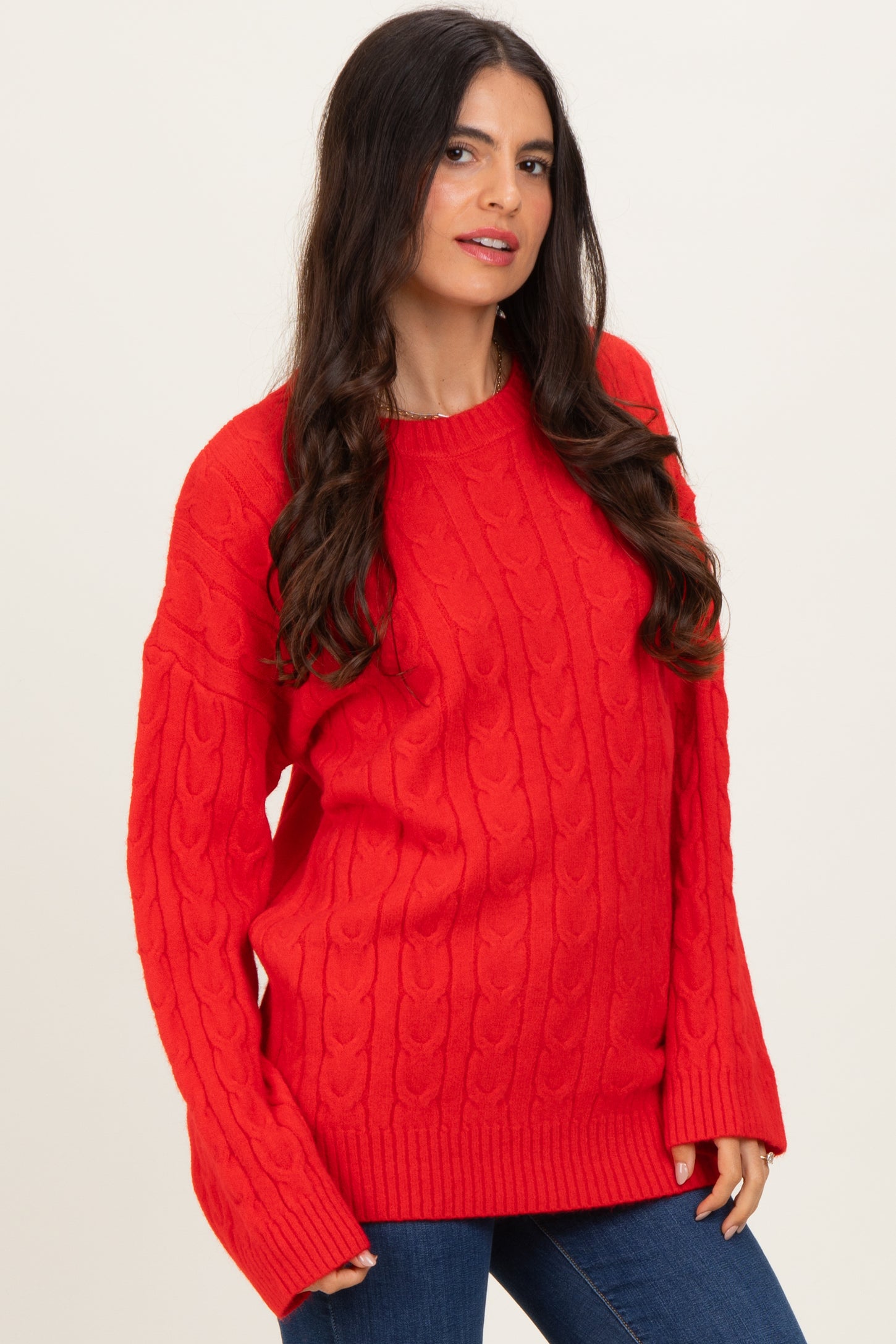 woman wearing a red cable knit sweater with long sleeves and ribbed hem paired with blue jeans