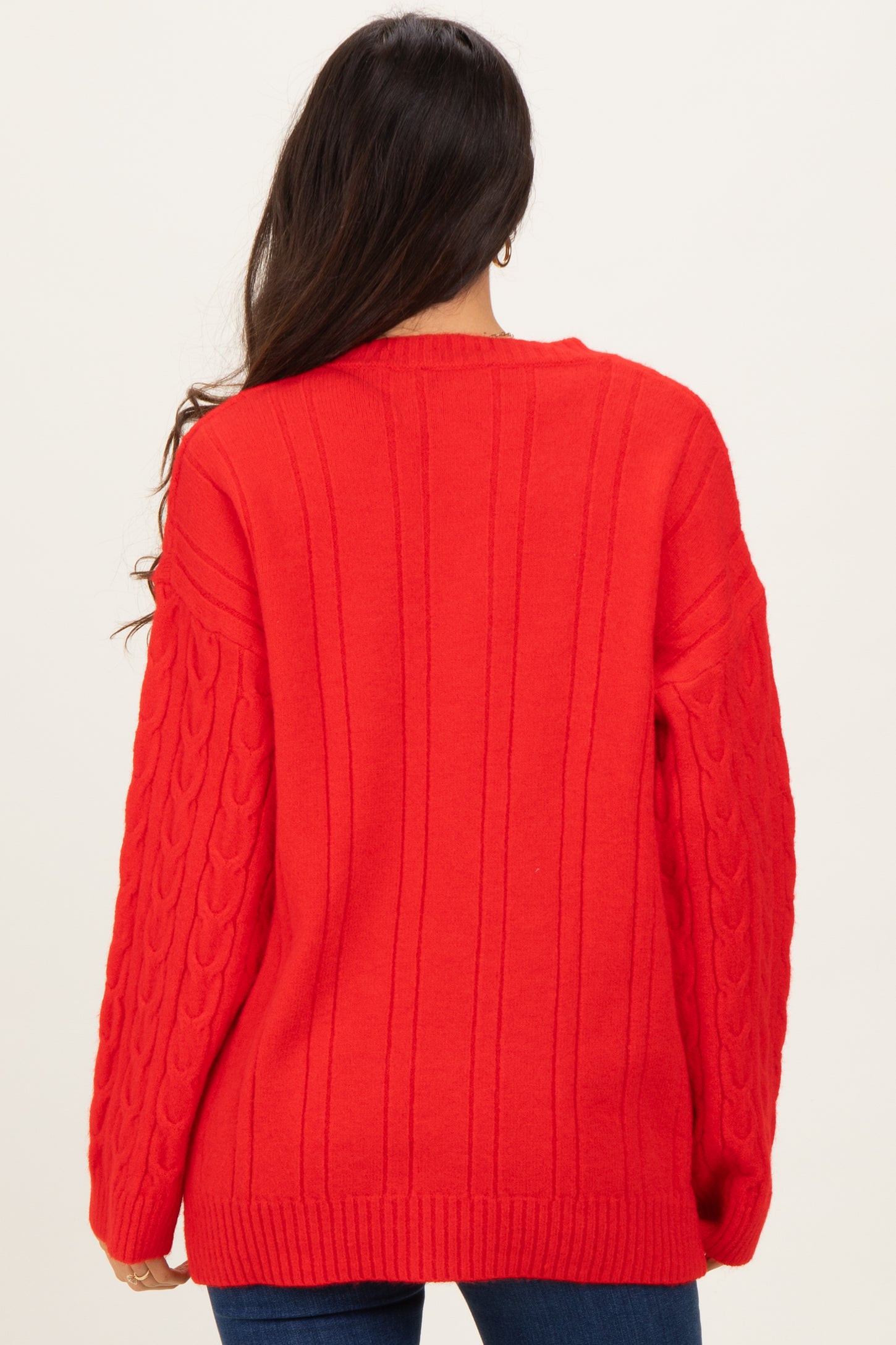 woman wearing a bright red oversized cable knit sweater with long sleeves and a scoop neckline, viewed from the back