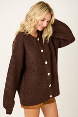 woman wearing a brown ribbed oversized cardigan with large buttons and long sleeves, smiling and touching her hair