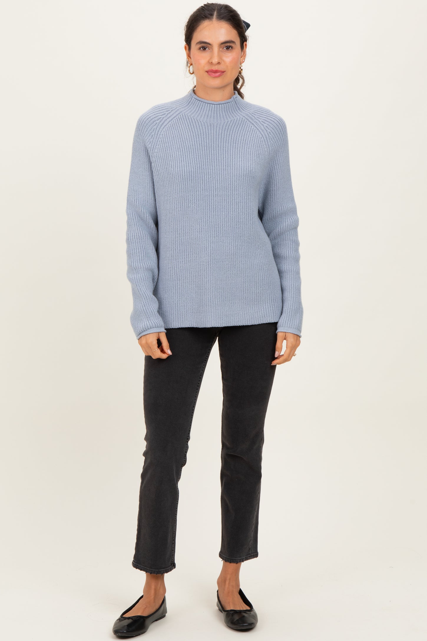 woman wearing a light blue ribbed sweater with long sleeves and black jeans, standing in a casual pose