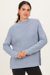woman wearing a light blue ribbed sweater with a high neckline and long sleeves, posing with a smile