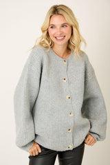 woman wearing a light grey oversized button-up sweater with ribbed texture and puffy sleeves