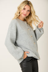 woman wearing a light grey cardigan with ribbed texture and wooden buttons, styled with black faux leather pants