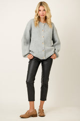 woman wearing a grey oversized knit cardigan with buttons and black faux leather cropped pants, styled with brown loafers